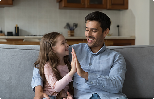 Smiling father and daughter high-five on a sofa.