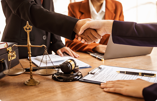  Business people shaking hands at a table with legal scales and a gavel.